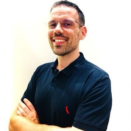 Person wearing a black polo shirt with arms crossed against a plain background.