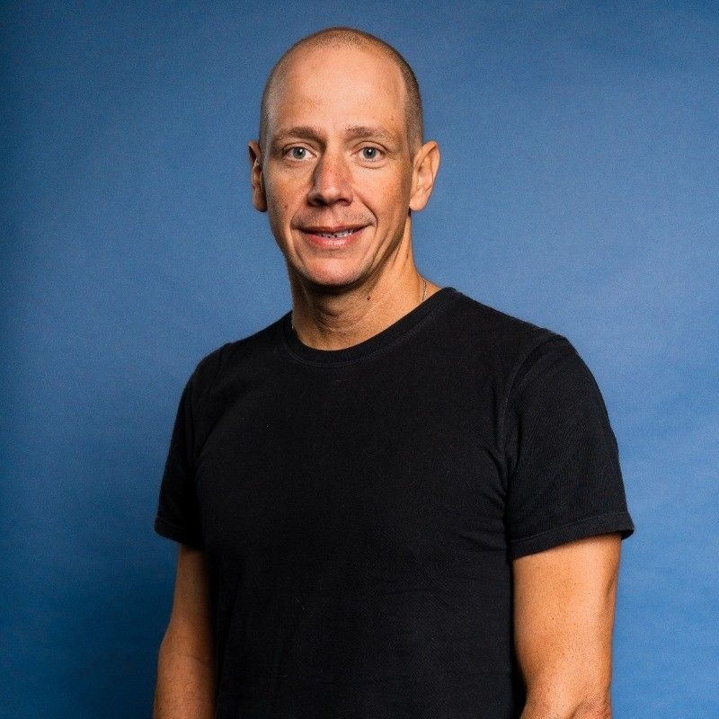 Person wearing a black t-shirt standing against a blue background.